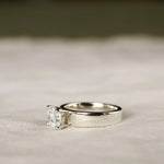 side view of chunky wide band engagement ring with cushion cut diamond and blurred background
