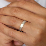 Close-up of a hand wearing a white gold 5mm brushed wedding ring on a plain background