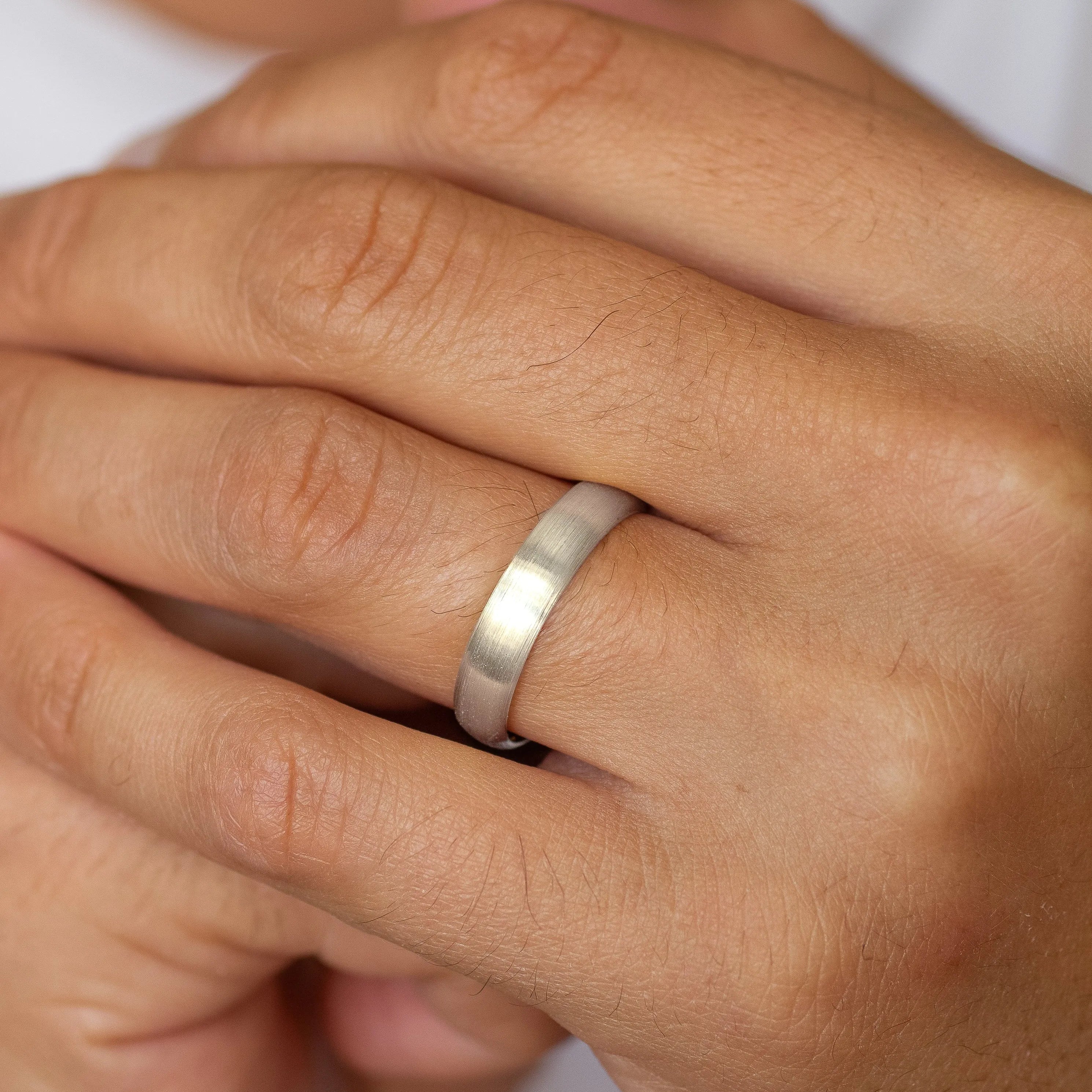 Close-up of a hand wearing a white gold 5mm brushed wedding ring on a plain background