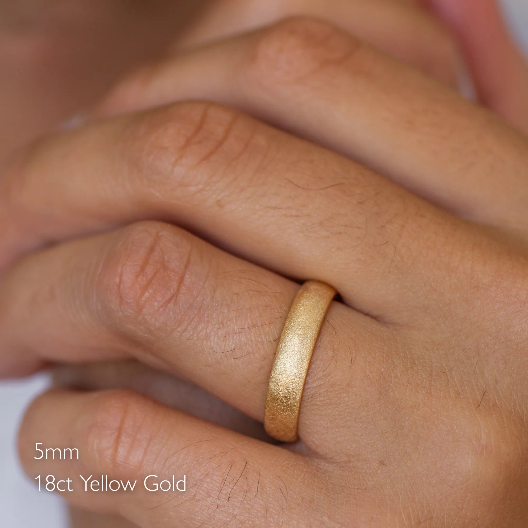 close up of male hand wearing 18ct yellow gold 5mm frosted wedding ring in d shape