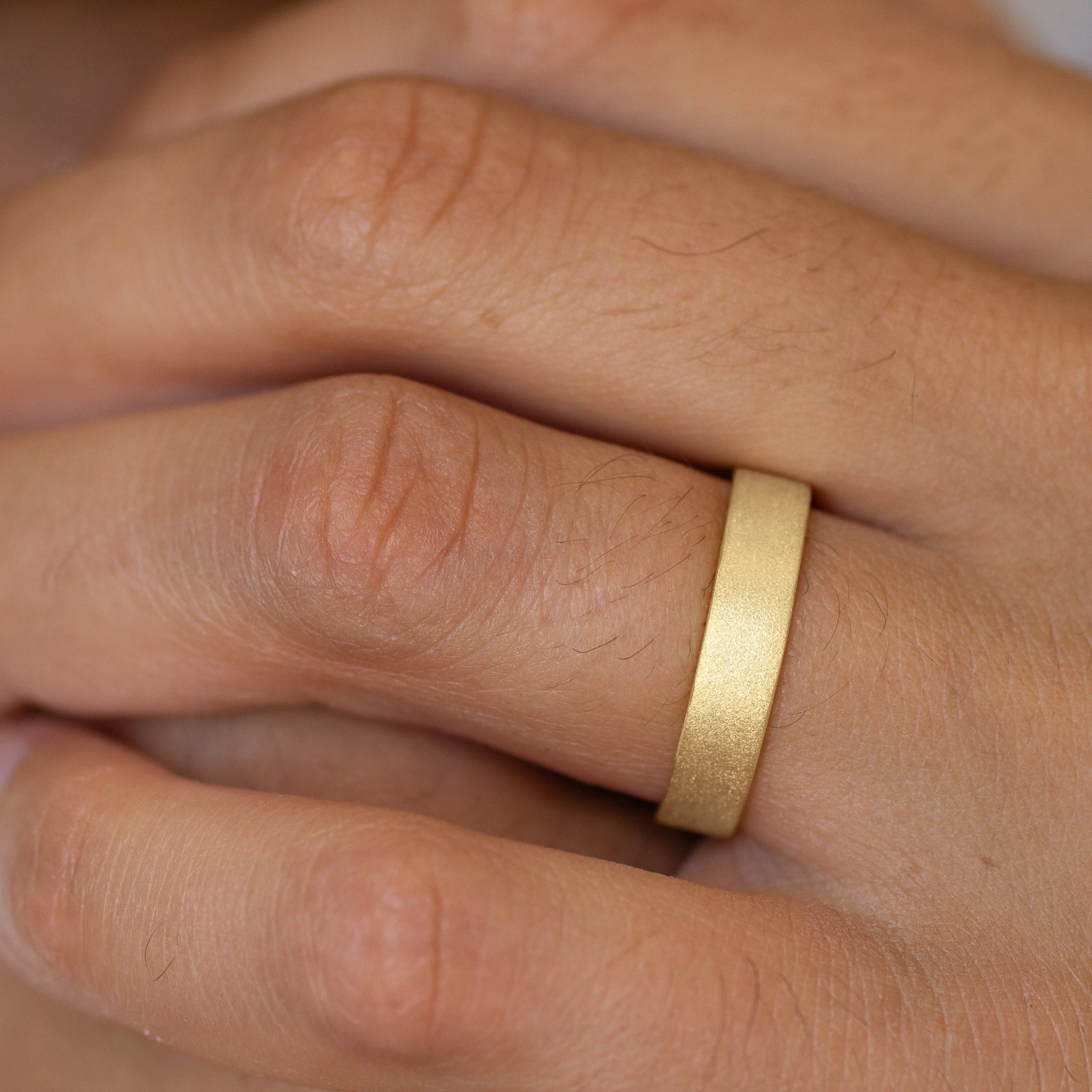 Close-up of a mens hand wearing a gold frosted matte wedding ring on a blurred background