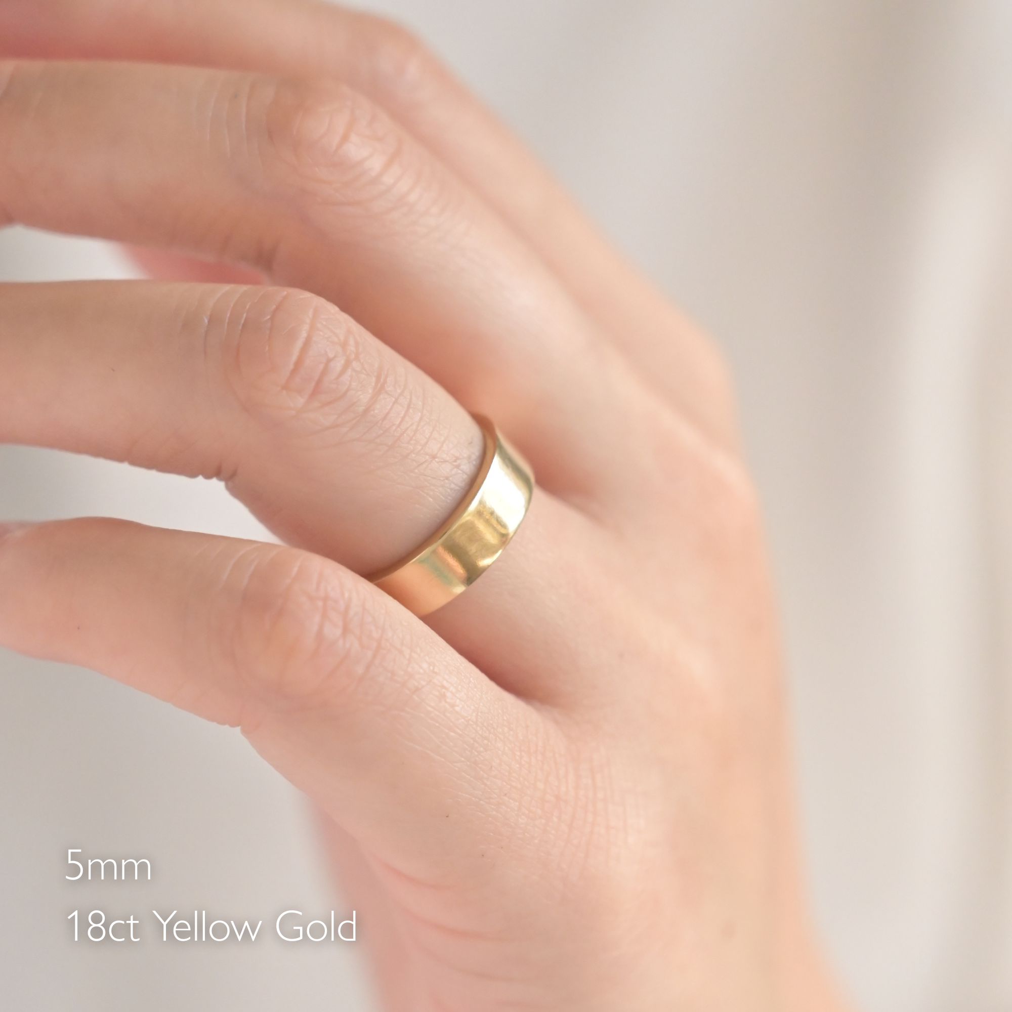 flat polished wedding ring ring on a woman's finger with '5mm 18ct Yellow Gold' text