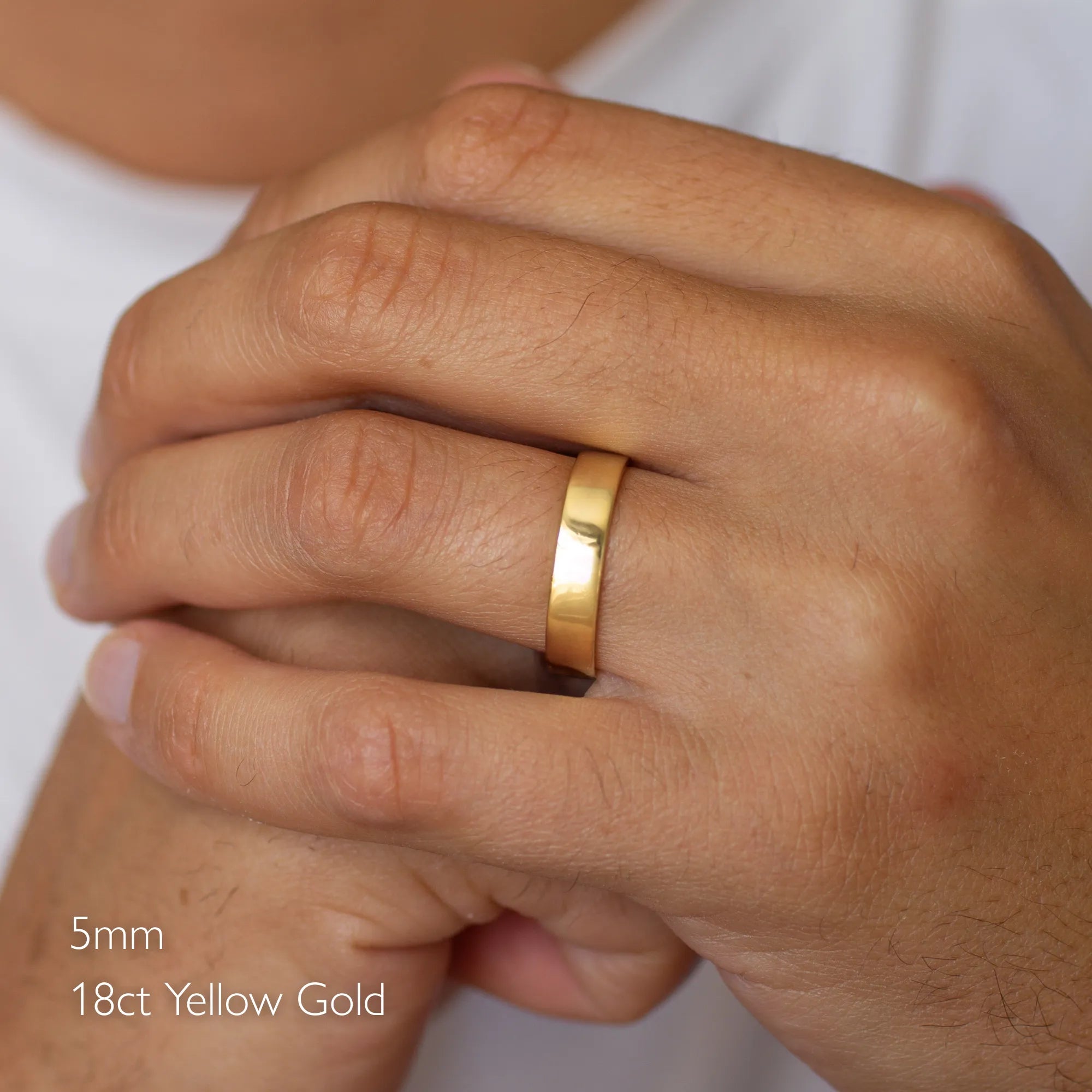 gold flat polished wedding ring on a person's finger with '5mm 18ct Yellow Gold' text.