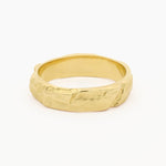 A textured gold ring with an organic, rough, hammered surface, shown on a clean white background.