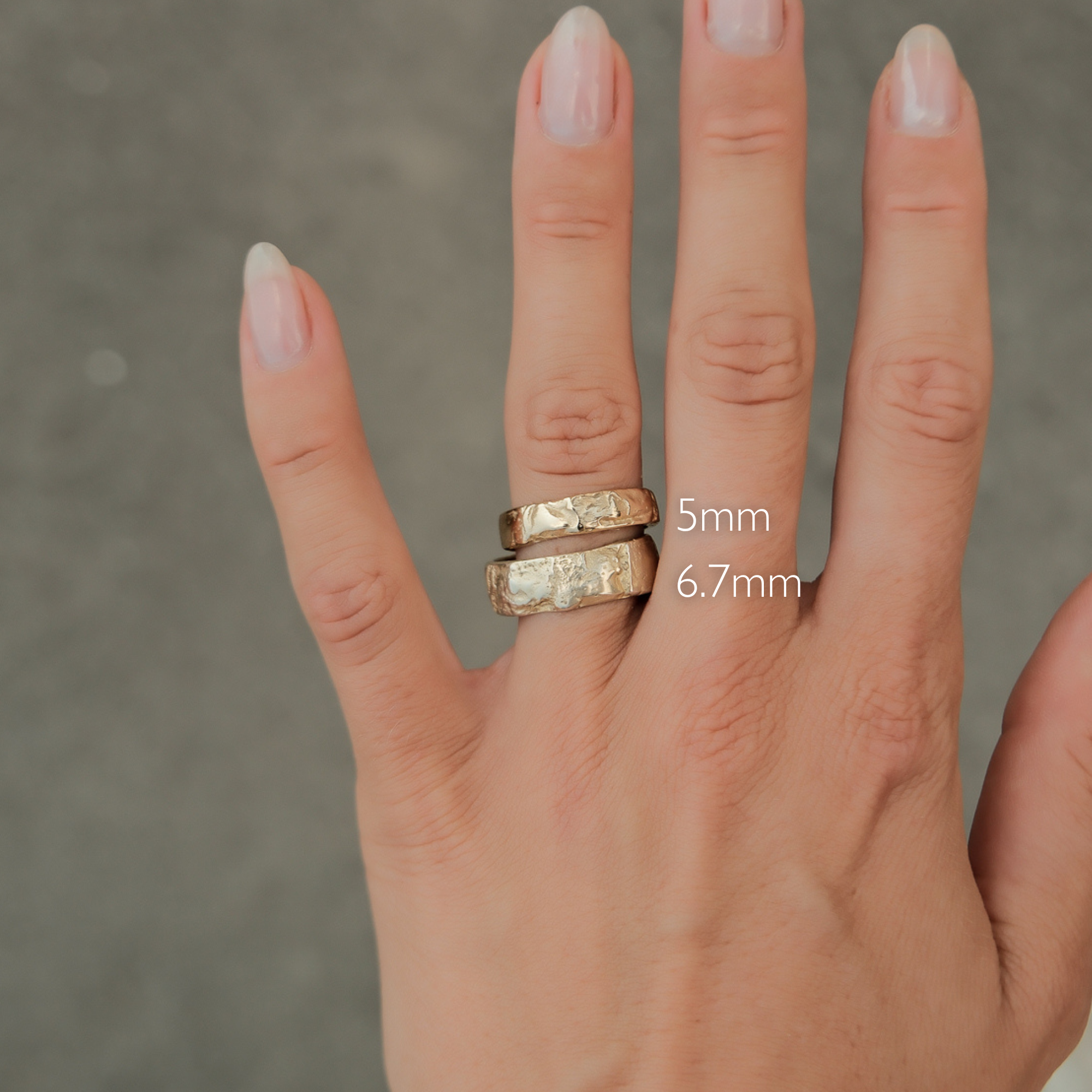 hand wearing two tree-bark textured wedding rings in gold in 5mm and 6.7mm to show width comparison