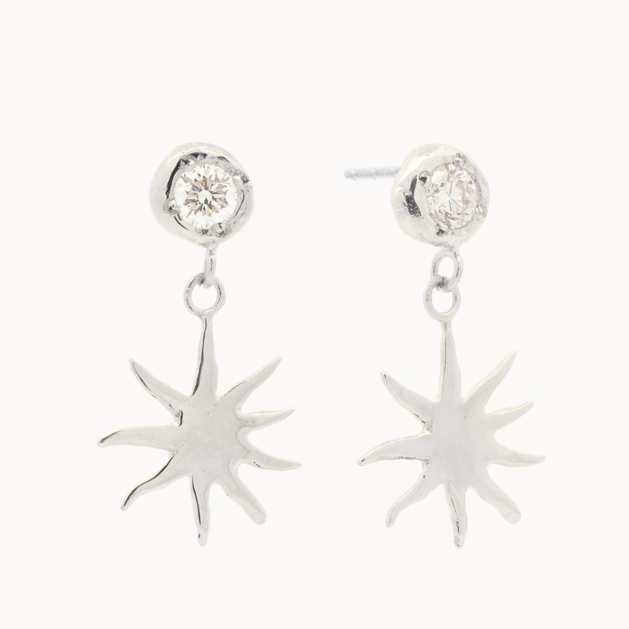 White gold diamond stud earrings with sun-shaped charms hanging off them against a white background