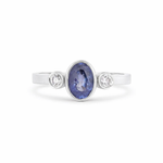 white gold bezel set blue sapphire trilogy engagement ring with diamonds on a white backdrop
