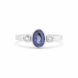 white gold bezel set blue sapphire trilogy engagement ring with diamonds on a white backdrop