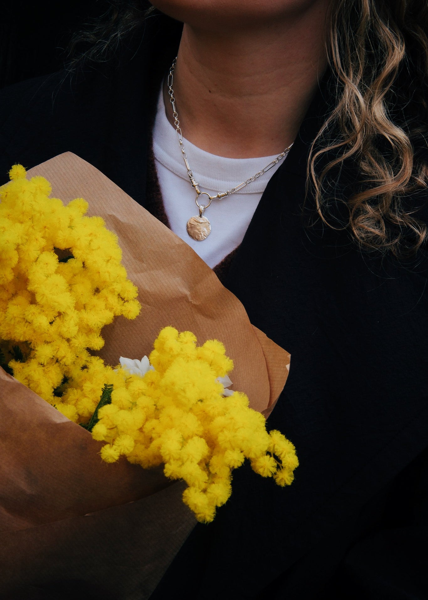 close up of person wearing chunky necklace and holding yellow flowers