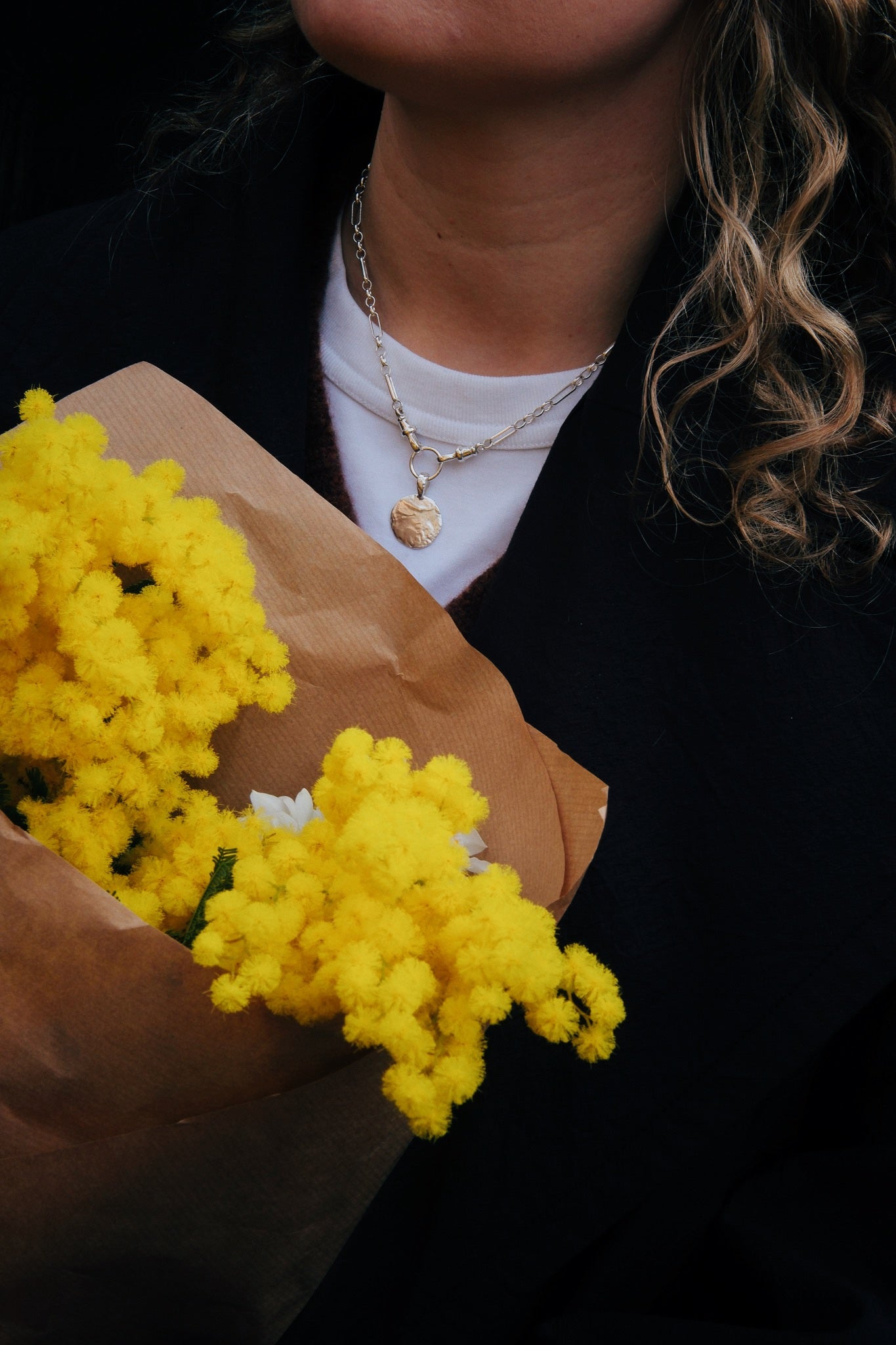 close up of person wearing chunky necklace and holding yellow flowers