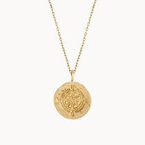 Gold necklace with a round compass pendant on a white background