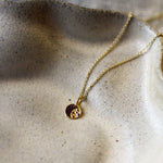 A delicate gold chain necklace with a small circular pendant resting on a textured beige ceramic dish.