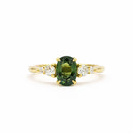 green oval sapphire engagement ring with tapered smaller diamonds on a gold band and white background