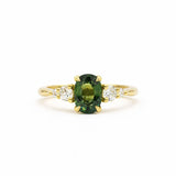 green oval sapphire engagement ring with tapered smaller diamonds on a gold band and white background