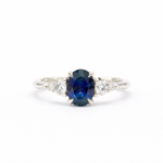 white gold engagement ring with a blue sapphire and two smaller diamonds on a white background