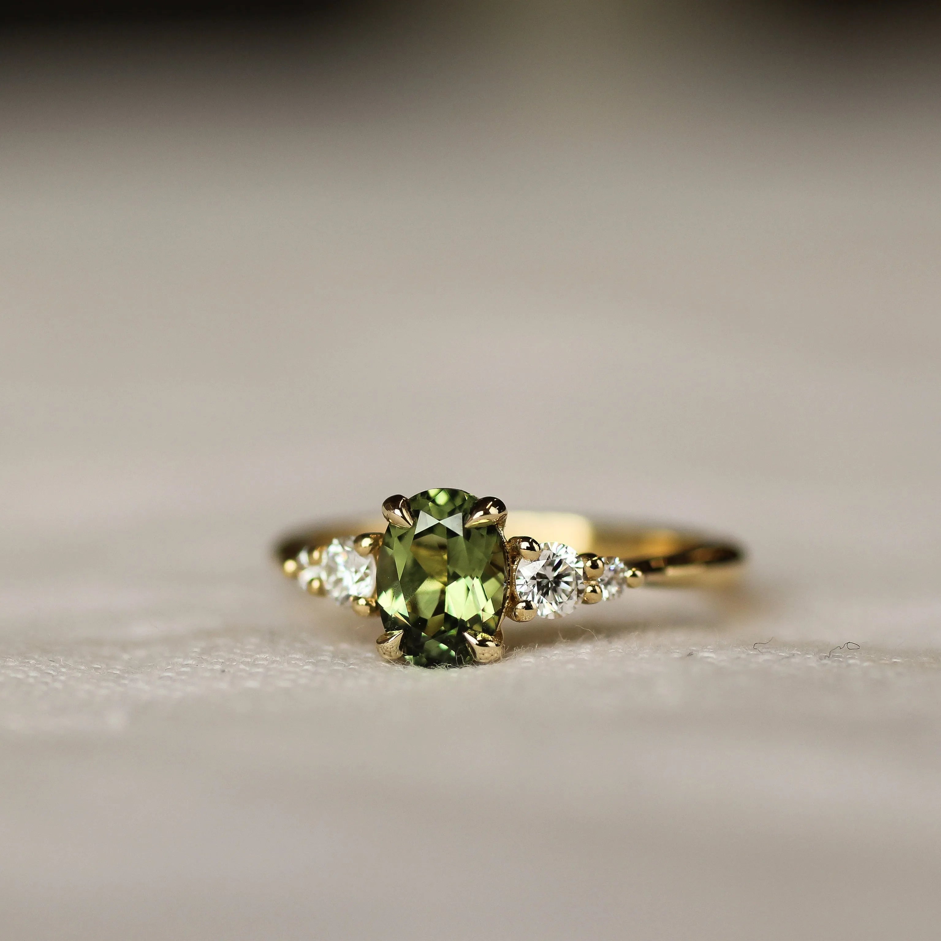Gold ring with light green gemstone and round diamonds on a beige surface