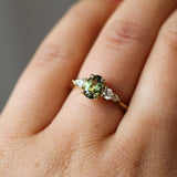 Close-up of a hand wearing a ring with a green gemstone on a neutral background