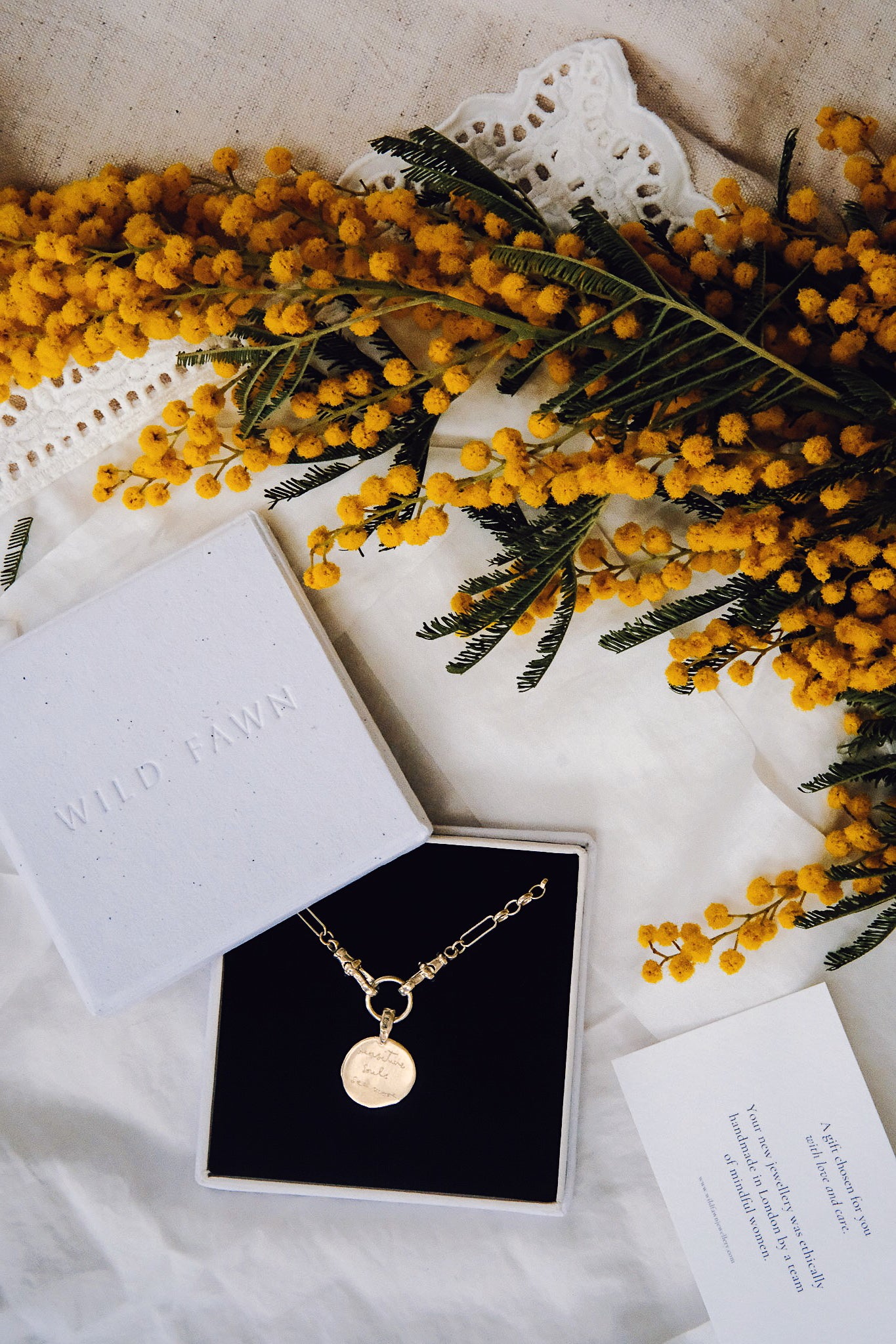 Gold necklace in an open jewelry box with yellow flowers on a textured surface