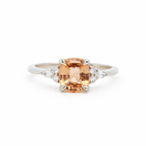 White gold engagement ring with a orange sapphire and round and pear diamonds on a white background