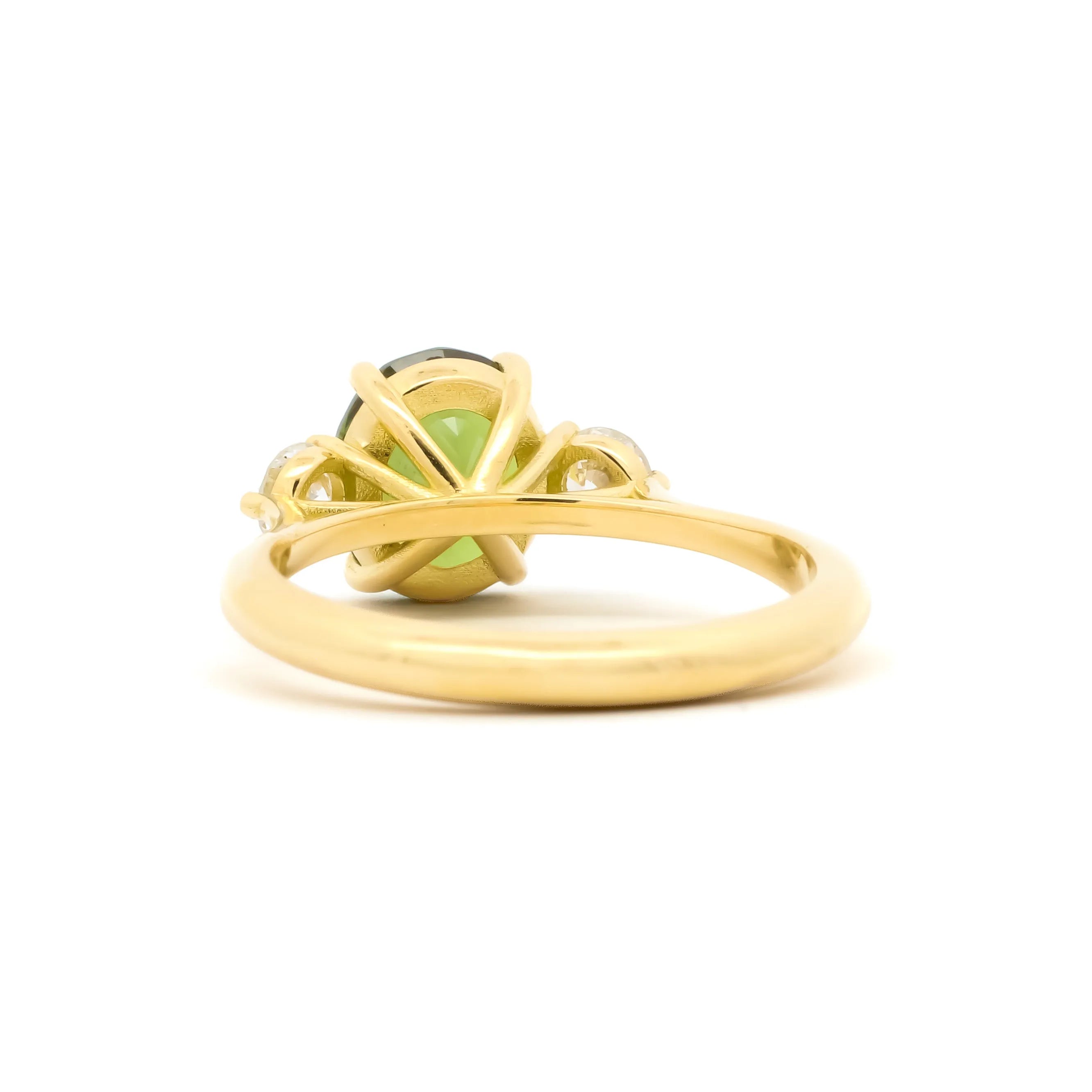 A yellow gold ring featuring a central light green gemstone surrounded by delicate gold filigree and small clear accent stones, shown on a plain white background.