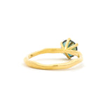 Back view of a gold ring with an organic-shaped band and a round blue green sapphire high-set with prongs against a white background