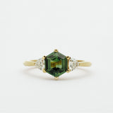 Gold ring with a green hexgaon sapphire and smaller triangular diamonds on a white background