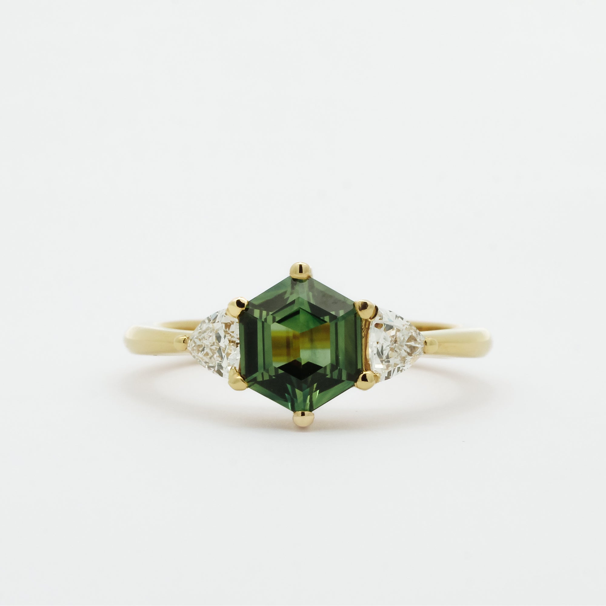 Gold ring with a green hexgaon sapphire and smaller triangular diamonds on a white background