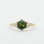 Gold ring with a green hexgaon sapphire and smaller triangular diamonds on a white background