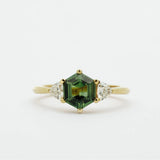 Gold ring with a green hexgaon sapphire and smaller triangular diamonds on a white background