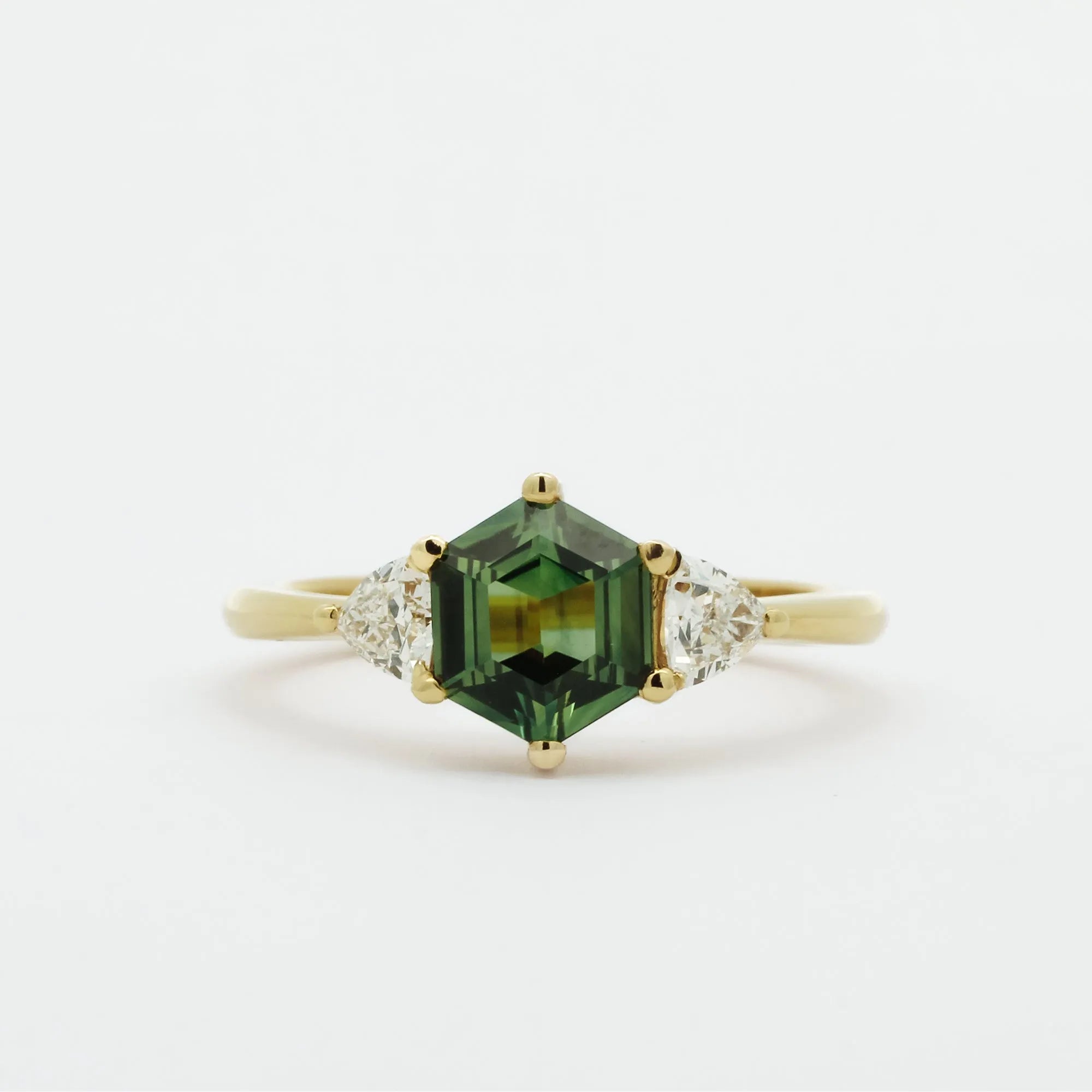 Gold ring with a green hexgaon sapphire and smaller triangular diamonds on a white background