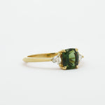 Gold ring with a green gemstone and diamond accents on a white background