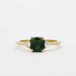 Gold ring with a green cushion cut sapphire and smaller triangle-shaped diamonds on a white background