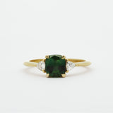 Gold ring with a green cushion cut sapphire and smaller triangle-shaped diamonds on a white background