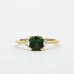 Gold ring with a green cushion cut sapphire and smaller triangle-shaped diamonds on a white background