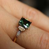 Gold ring with a green gemstone on a finger