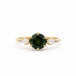 Gold engagement ring with a green round sapphire and smaller kite-shaped diamonds on a white background