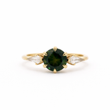 Gold engagement ring with a green round sapphire and smaller kite-shaped diamonds on a white background