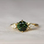 Gold ring with a green gemstone and kite-shaped diamonds on a light background