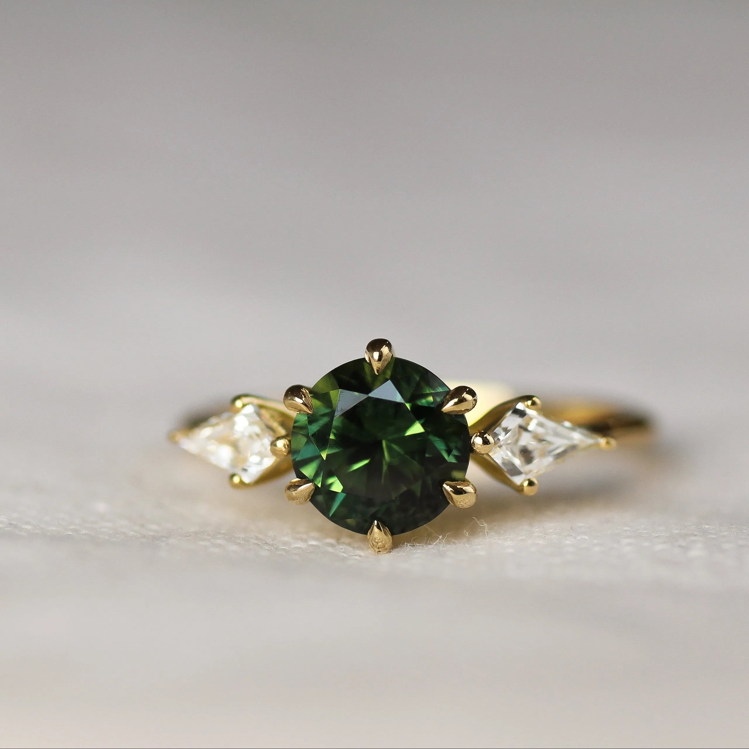 Gold ring with a green gemstone and kite-shaped diamonds on a light background