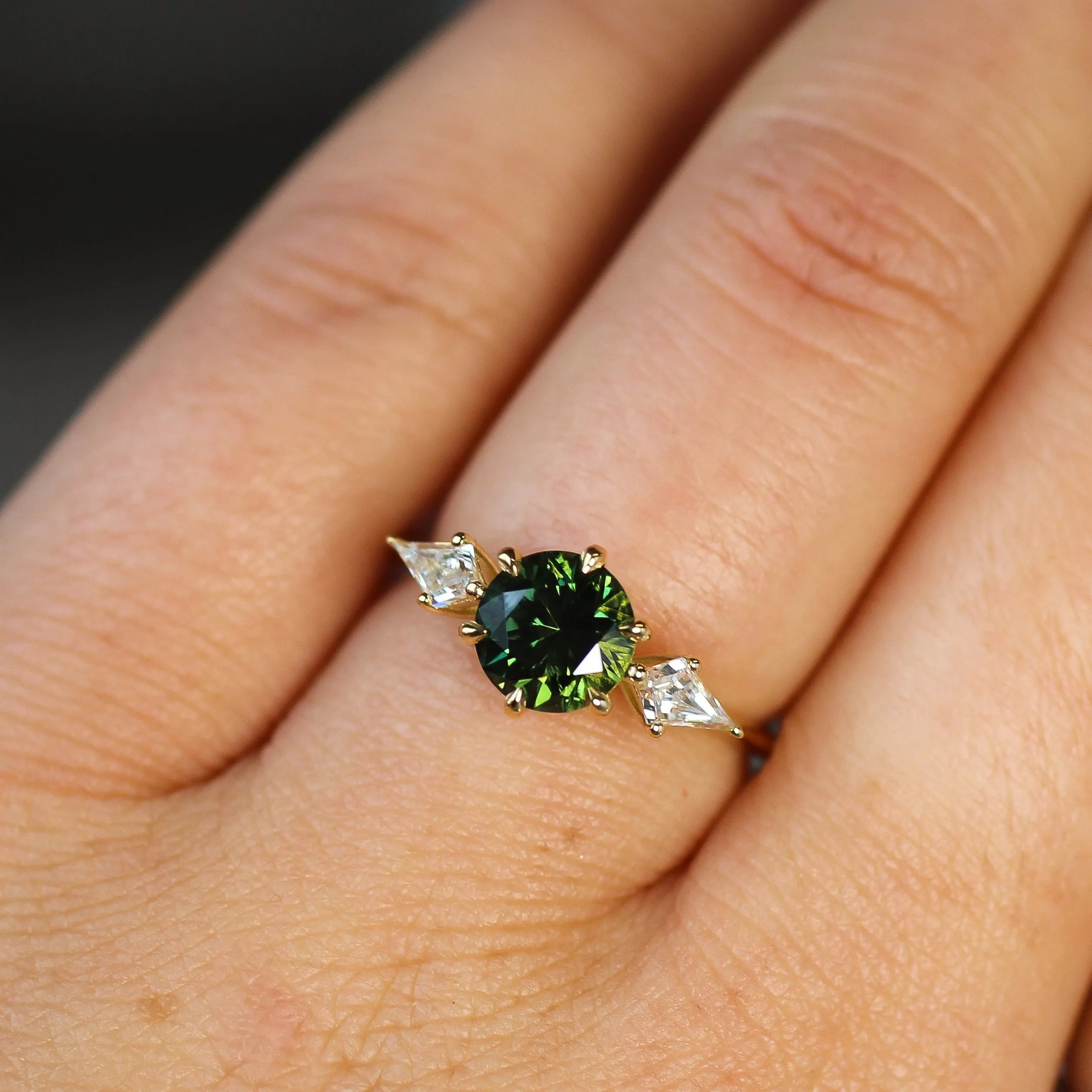 Ring with a round green gemstone and kite-shaped diamond accents on a hand