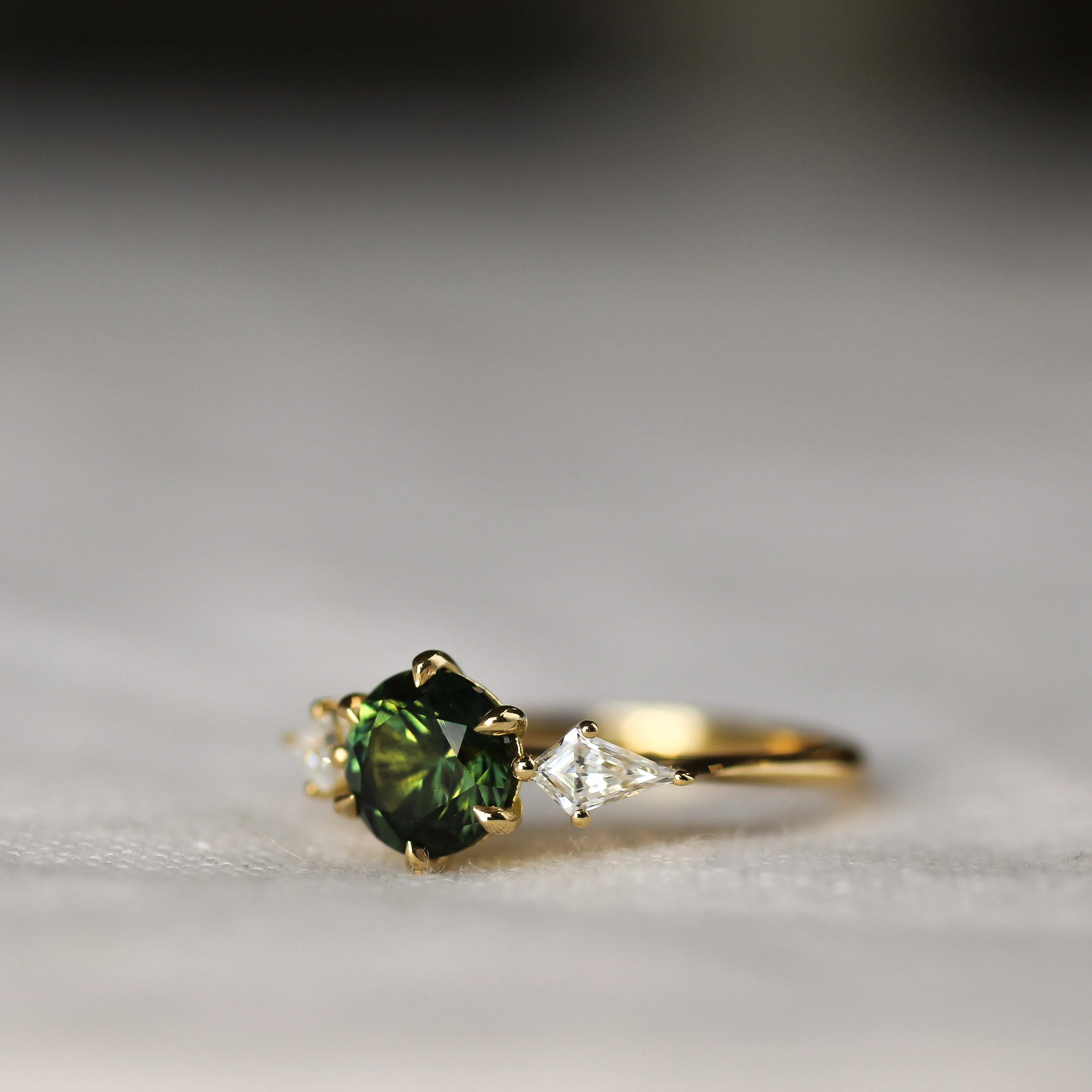 Gold ring with a green gemstone on a light gray background