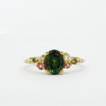 Gold ring with a green gemstone and smaller pink and diamonds on a white background