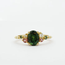 Gold ring with a green gemstone and smaller pink and diamonds on a white background