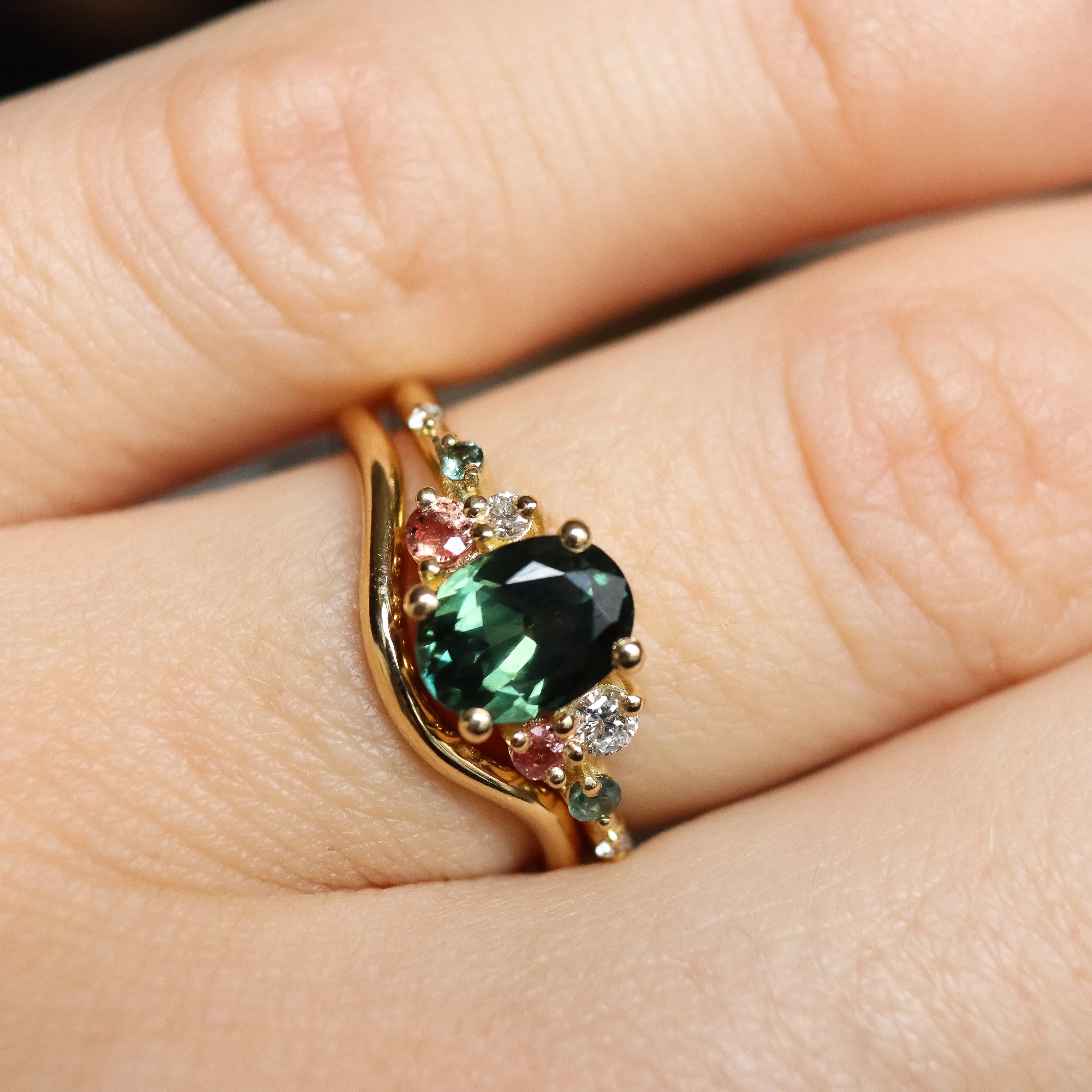 Gold ring with a green gemstone on a hand with wedding ring