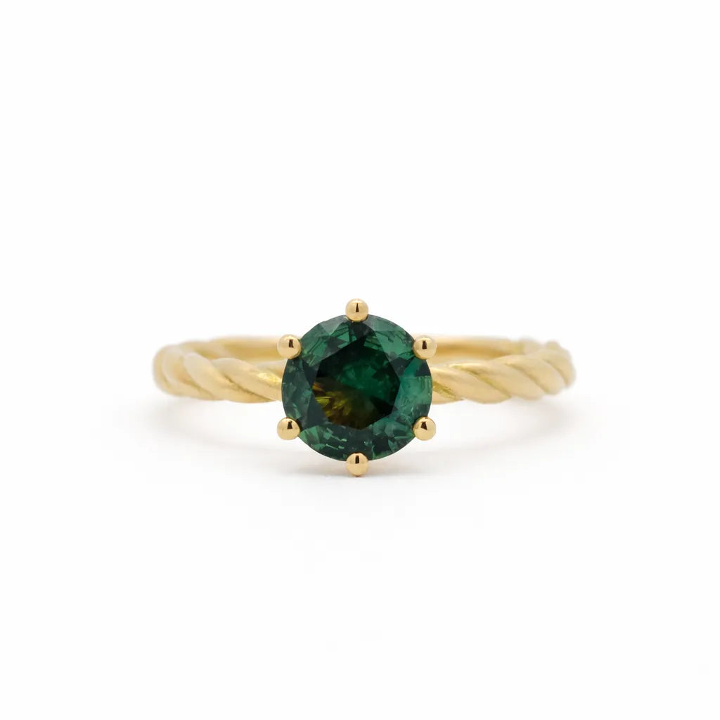 Gold engagement ring with a green round sapphire and twisted shank on a white background