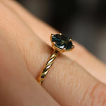 Gold ring with a green gemstone on a finger against a blurred background