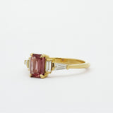 Gold ring with a peachy berry pink gemstone on a white background