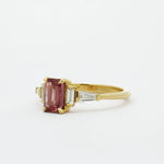 Gold ring with a peachy berry pink gemstone on a white background