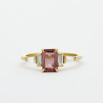 Gold ring with a pink sapphire and baguette diamonds on a white background