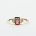 Gold ring with a Padparadscha pink sapphire and baguette diamonds on a white background